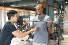 smiling-black-man-lifting-barbell-with-personal-trainer.jpg